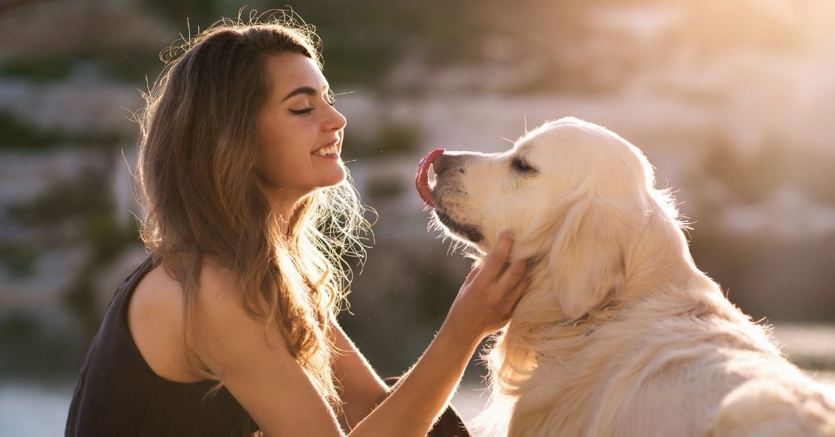 A woman in the sunshine smiling while gently interacting with a golden